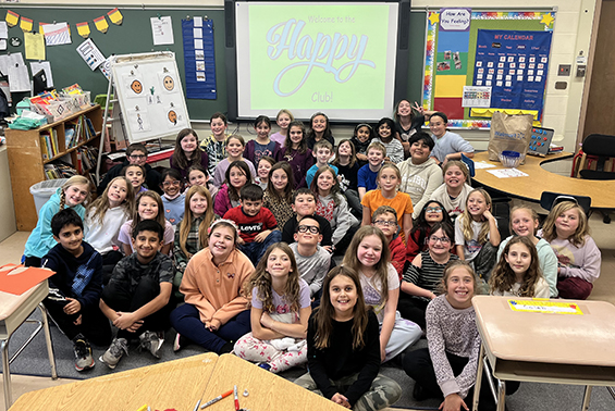 a group of students sitting on the floor with the Happy Club on the computer screen