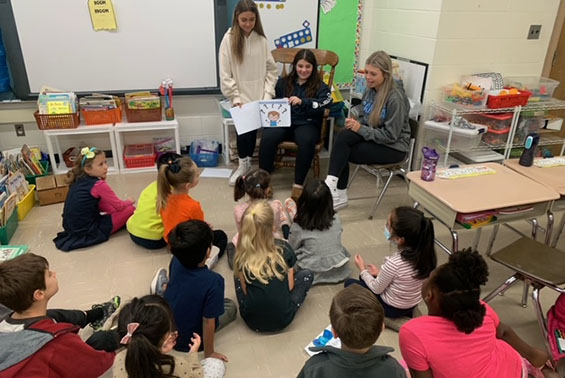 Older students reading book to younger students