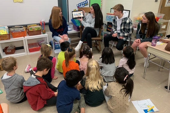 Older students reading book to younger students