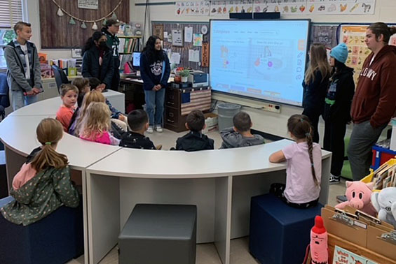 Older students reading book to younger students