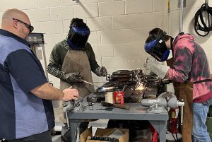 Two students welding while teacher supervises